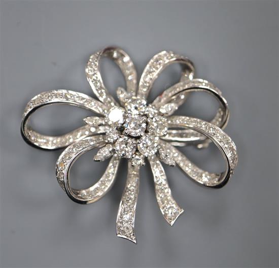 A mid 20th century white metal and diamond cluster set ribbon scroll brooch, 36mm, gross 15.6 grams.